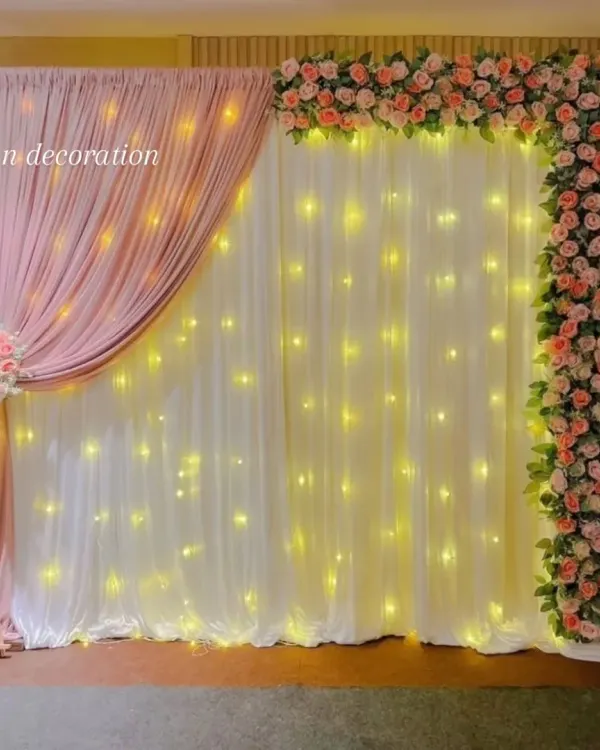 An elegant photo backdrop created with drapes and artificial flowers. I used a combination of white and pink fabric with warm fairy lights and a floral border for a soft, classic look.