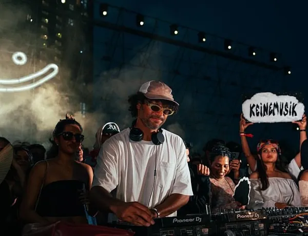 The vibe is everything. Here's &ME of the Keinemusik crew at the decks, with the iconic smiley logo and a fan holding a "Keinemusik" sign. This is the authentic, community-driven atmosphere I cultivate.