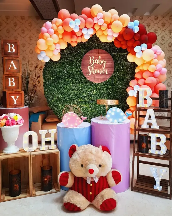 A colorful and fun baby shower setup. This design features a vibrant balloon arch, a green wall backdrop, and playful elements like a teddy bear and "Oh Baby" letter blocks.