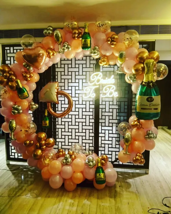 A fun and bubbly "Bride To Be" party setup. This circular balloon arch in pink and gold is decorated with champagne bottle and ring-shaped foil balloons, perfect for a bachelorette party or bridal shower.