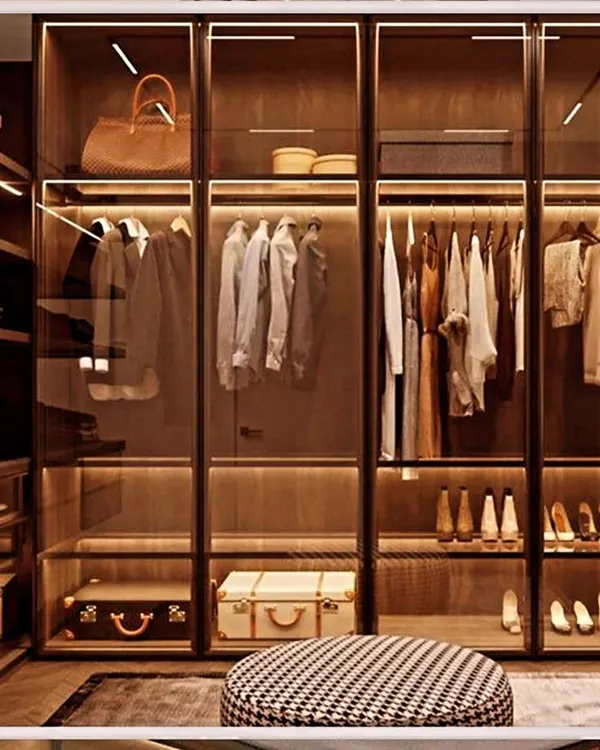 A beautifully styled walk-in closet featuring profile glass doors and warm LED lighting. This design turns your wardrobe into a personal showroom, keeping everything visible and organized.