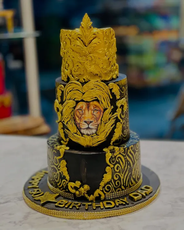 A majestic cake for a dad who is the king of the family. This three-tier black and gold cake features intricate baroque details and a powerful lion face, symbolizing strength and royalty.