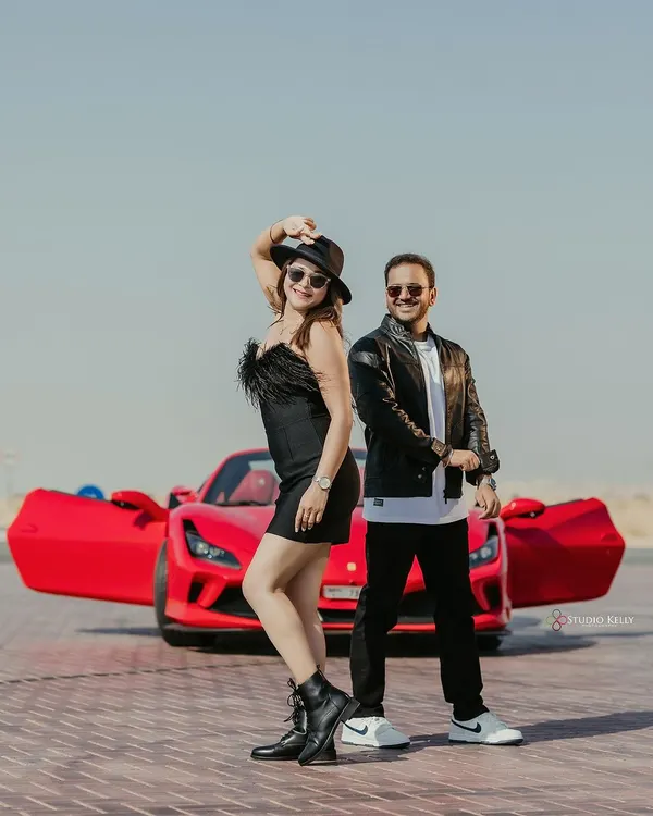 A cool, edgy pre-wedding shot in the Dubai desert featuring a vibrant red Ferrari. The couple's leather jackets and confident poses create a powerful, movie-poster look.