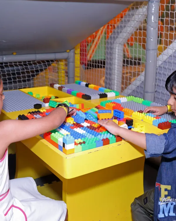 Two children collaborate at the Lego table, building colorful structures and developing teamwork skills.