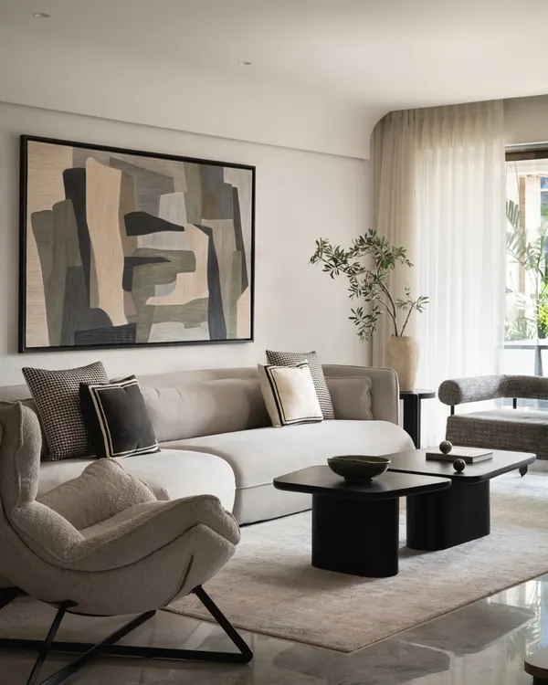 This living room captures the essence of quiet luxury. The custom 12-foot angular sofa in light grey boucle fabric creates an inviting space for connection, while the large monochrome artwork adds a layer of personal, artistic flair. Every element, from the textured armchair to the bold black coffee tables, is chosen to build a harmonious and sophisticated residential interior.