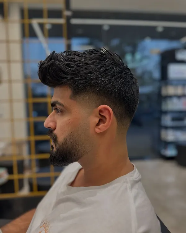 This is a classic example of a mid-fade. Notice the seamless blend from the shorter sides to the longer, textured hair on top, paired with a neatly shaped beard. This is a versatile and popular men's hairstyle.