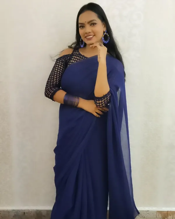 A modern and chic party look featuring a stunning royal blue saree. The makeup is bold and confident, with a focus on flawless skin and matching blue accessories.