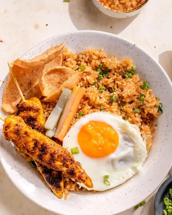 A complete Indonesian Nasi Goreng experience on a plate. This dish features fragrant fried rice, perfectly grilled chicken satay skewers, a sunny-side-up egg, and crispy prawn crackers, served with our secret recipe sauces.