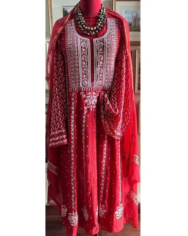 This regal Sindoori Red Anarkali is a masterpiece of celebration wear. Crafted from fine Mul fabric, it features a symphony of intricate Chikankari, Kutdana, Poth, and sequin embellishments, making it a statement of timeless elegance.