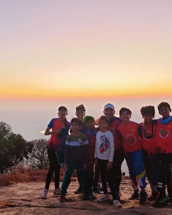 A group of young campers stands together against a beautiful sunrise at Skandgiri. Our camps are designed to inspire a love for nature and create unforgettable moments like this.