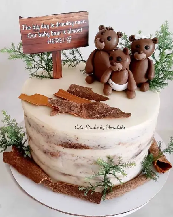 A very cute and rustic baby shower cake. The sign says 'Our baby bear is almost here,' and the cake is decorated with cinnamon sticks and little bear figurines.