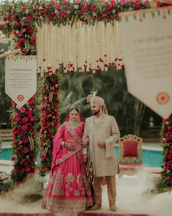 The couple stands united under a magnificent floral mandap, a portrait of grace and togetherness just after their Varmala exchange. The soft smoke at their feet adds a touch of magic to this traditional wedding photograph.