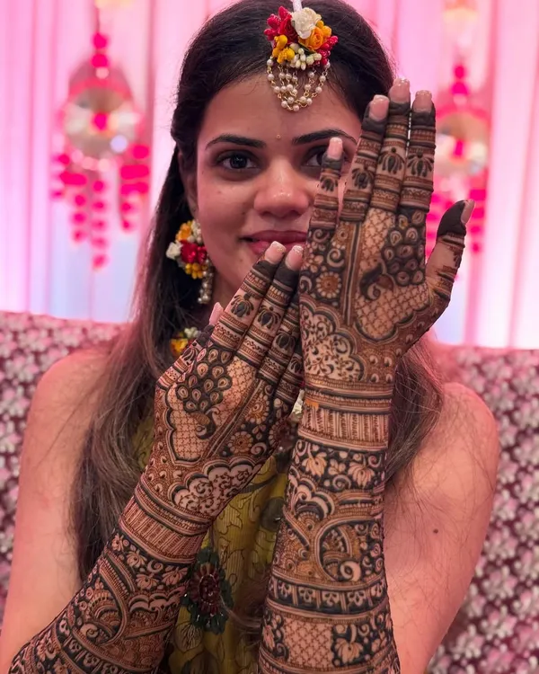 A beautiful bride, adorned with floral jewelry, proudly showing her intricate bridal mehendi. Her happy smile is the best reward for my work.