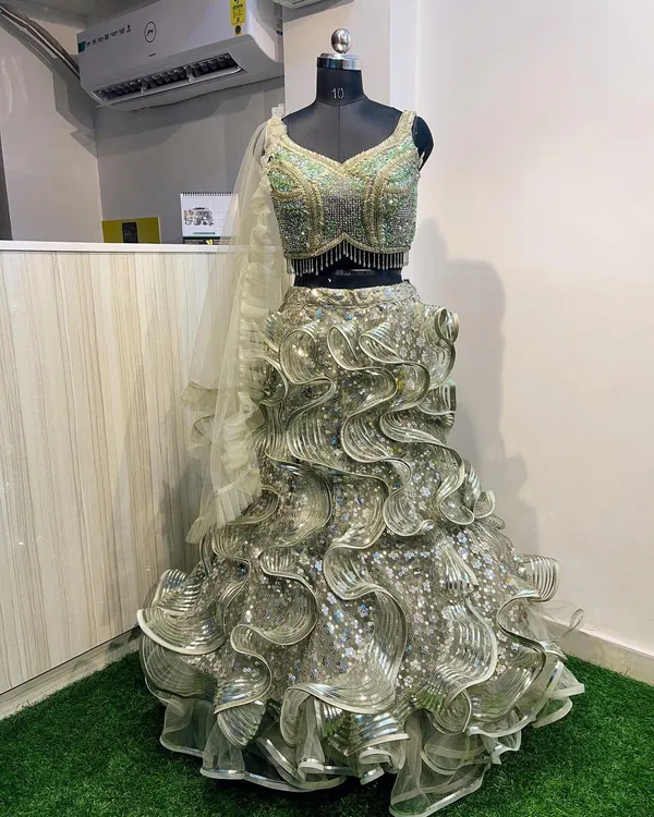 This modern green and silver ruffled lehenga is a true statement piece, perfect for a reception or cocktail party. The heavily embellished blouse features intricate beadwork and sequins, while the multi-layered ruffled skirt creates dramatic volume and movement.