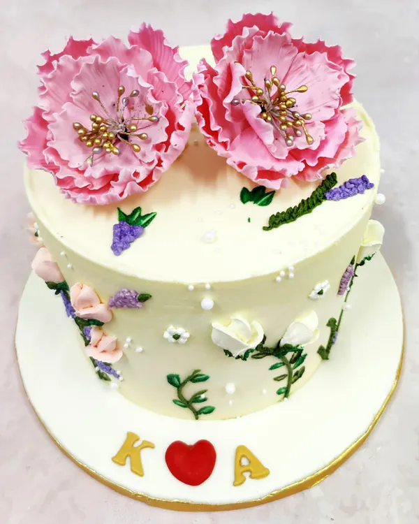 We paint a picture of romance with this hand-painted flower cake. Delicate pink blooms, resembling peonies, crown the cake, while smaller blossoms and leaves are artfully painted onto the buttercream, creating a piece of edible art for an intimate celebration.