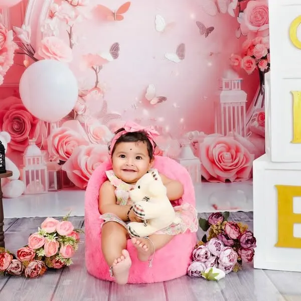 A joyful first birthday portrait set against a custom pink floral backdrop. The stacked 'ONE' blocks clearly mark the occasion, while the baby's happy expression is the true centerpiece of the photo.