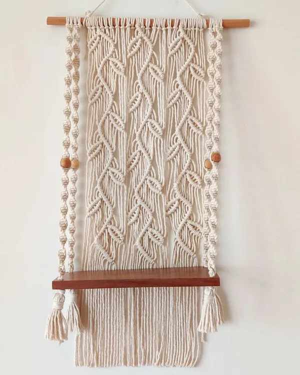 I designed this macrame wall shelf with a beautiful leafy vine pattern as the backdrop. The sturdy wooden shelf is perfect for holding small plants, books, or even creating a small, peaceful mandir space in your home.