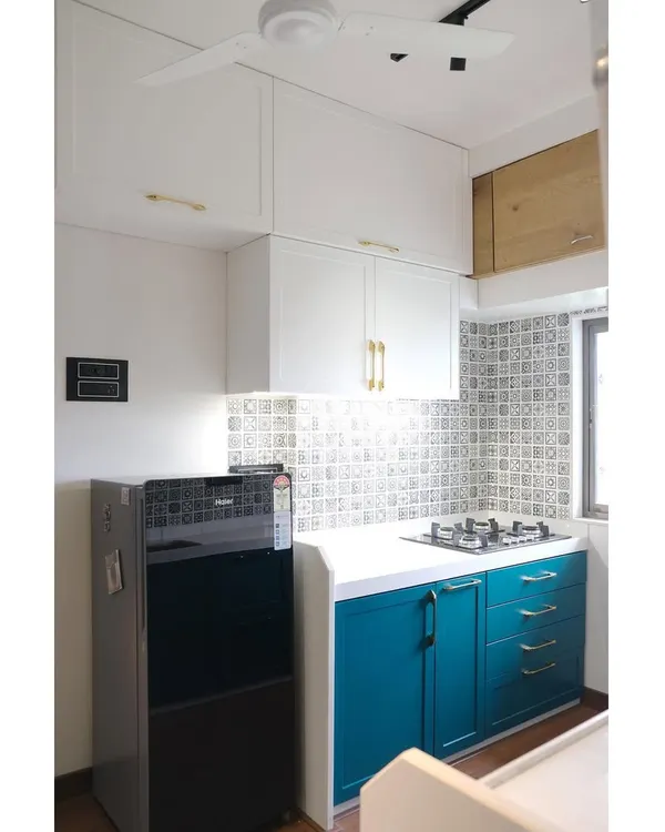 This kitchen for influencers Abhi and Niyu features a beautiful dual-tone design with a rich teal PU finish on the lower cabinets and classic white uppers, complemented by elegant brass handles.
