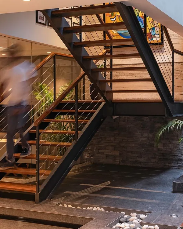 A staircase should be more than just functional; it should be a sculptural element. This design integrates seamlessly with the living space, featuring an indoor court with pebbles and greenery below, bringing light and life into the home's core.