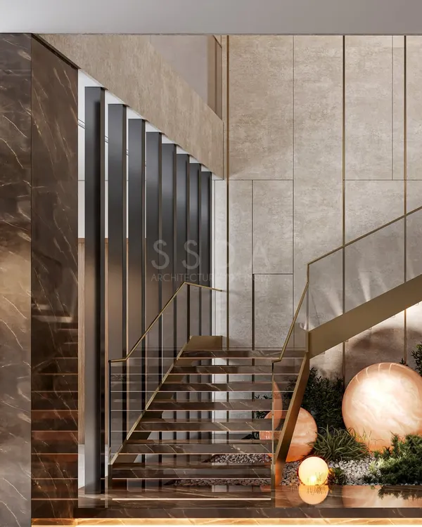 This staircase is designed as a sculptural feature, with golden accents that shimmer against the neutral stone palette. Lush greenery beneath softens the formality, infusing the space with freshness and calm.