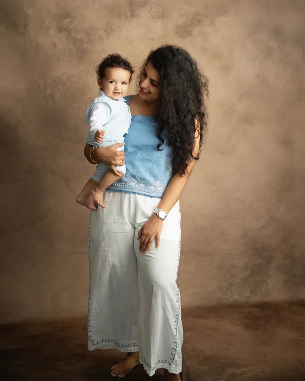 A mother's gentle gaze at her smiling baby. This classic studio portrait, with its warm brown backdrop, beautifully highlights the love and connection between them.
