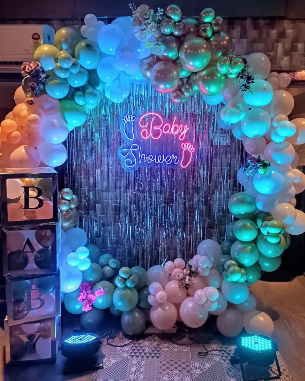 This is one of my most popular baby shower designs. I combine a full ring of pastel and chrome balloons with a silver shimmer wall and a bright neon sign to create the perfect photo spot for the parents-to-be.