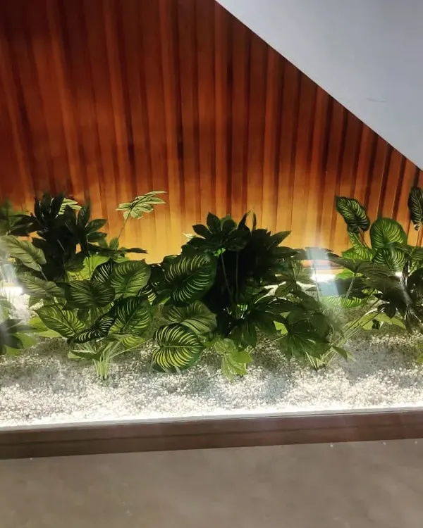 We turned this unused space under a staircase into a beautiful indoor garden. Using a bed of white pebbles and a variety of artificial plants with large leaves, we created a focal point that is both elegant and maintenance-free.