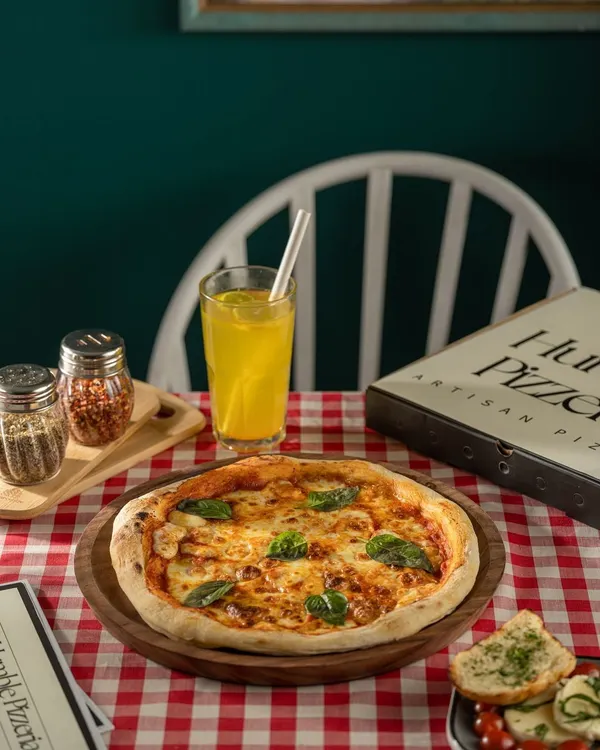 A classic Margherita pizza for The Humble Pizzeria, set in a traditional cafe scene with a red checkered tablecloth. This shot evokes a sense of authentic, comforting Italian-American dining.