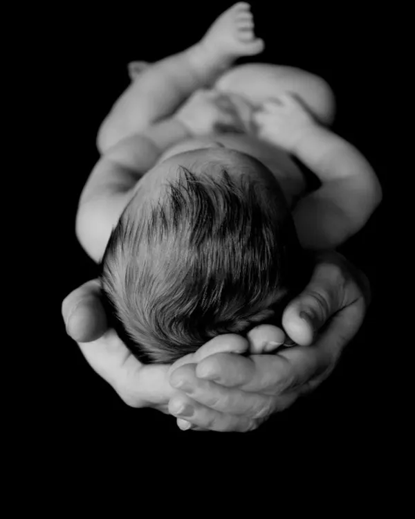 Cradled in loving hands. This powerful black and white newborn portrait emphasizes how small and precious your baby is, creating a deeply emotional and artistic photograph.