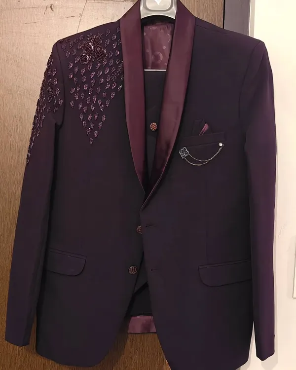 This is a stylish three-piece suit in a deep wine color, available for rent. It features unique shoulder detailing and a matching vest, perfect for making a statement at a wedding or pre-wedding shoot.