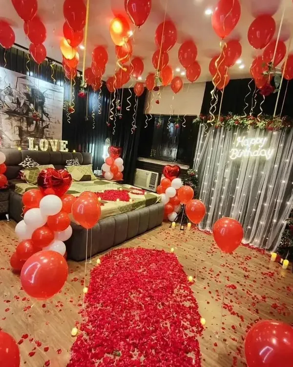 This is our ultimate romantic room decoration, perfect for a birthday or anniversary. It features a floor covered in red rose petals, dozens of red and white balloons, and a "Happy Birthday" neon sign against a lit-up backdrop.