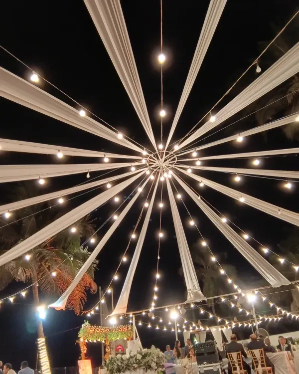 A stunning starburst canopy of white drapes and Edison bulbs. This design creates a spectacular focal point over a dance floor or seating area for an outdoor evening event.