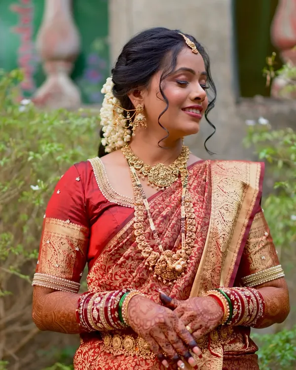 A beautiful South Indian inspired bridal look. The bride is wearing a stunning red and gold silk saree, with traditional temple jewelry and a classic updo adorned with jasmine flowers.
