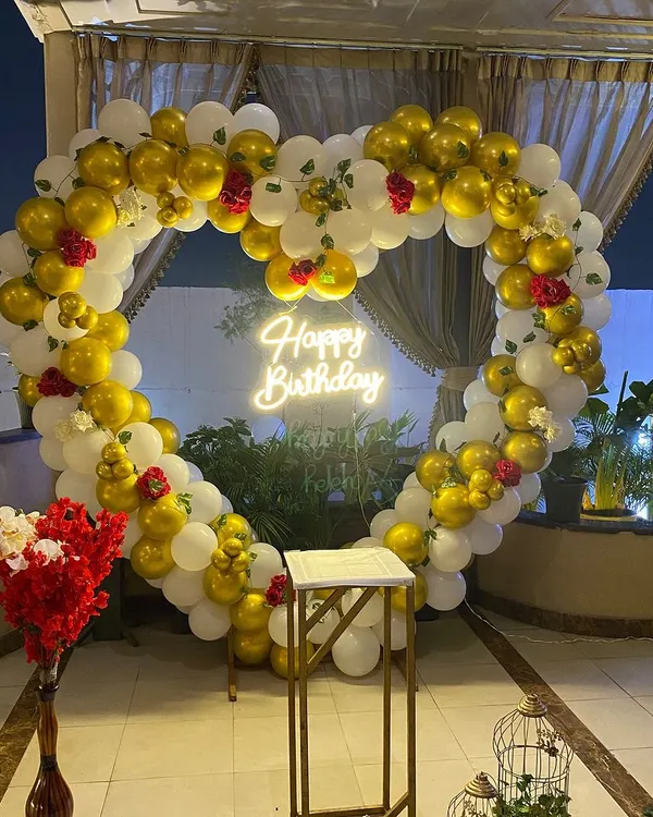 A large, perfectly shaped heart balloon arch made with gold and white balloons and decorated with small red roses. It's a showstopper for any romantic event.