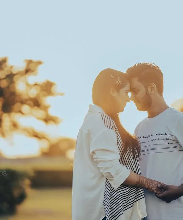A quiet moment as the sun sets. This golden hour engagement photo uses the soft backlight to create a beautiful silhouette effect, highlighting the couple's connection as they hold hands and touch foreheads.