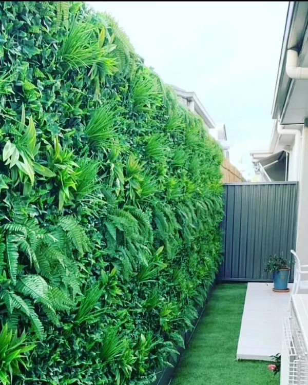 A dense, jungle-style vertical garden installed along a narrow walkway. This design uses a variety of artificial ferns and leafy plants to create a rich, textured look that provides privacy and greenery.