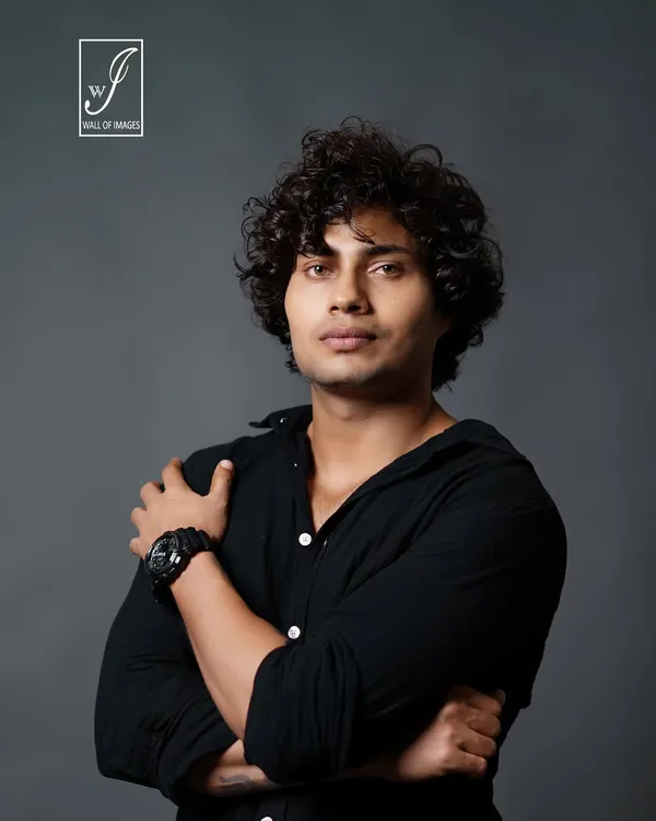 A strong male headshot. The direct eye contact and crossed arms convey confidence, while the studio lighting defines his facial structure.