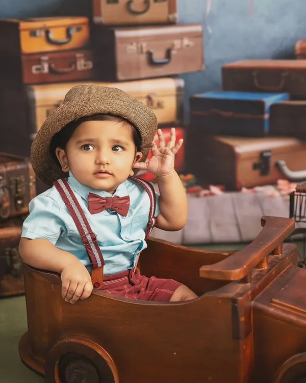 Waving goodbye to the baby days. This little traveler, complete with a hat and bowtie, is ready for his next big adventure in this vintage-themed studio shoot.