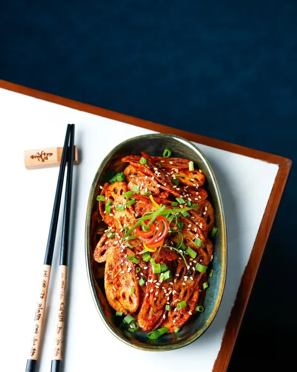 Crispy honey chilli lotus stem, shot with a dark, moody aesthetic to highlight its texture and colour.
