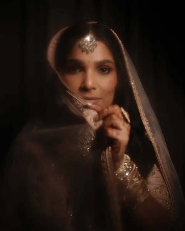 This is the epitome of timeless bridal elegance. Set against a dark, moody backdrop, her soft golden eye makeup and luminous skin create a dreamy, ethereal effect. Her hair is styled in a classic half-down look, perfect for her pastel pink lehenga.