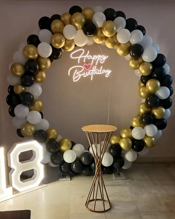 A classic black, white, and gold ring setup for an 18th birthday, complete with a neon sign, marquee numbers, and a cake stand.