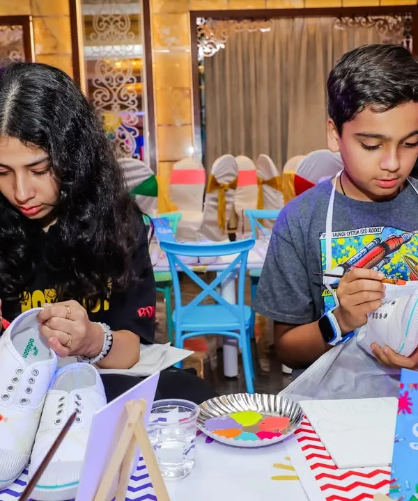 Kids deeply focused on painting their own canvas shoes. This DIY activity is a fantastic way for them to express their creativity and take home a unique, wearable souvenir.