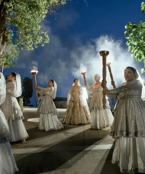 A dramatic and opulent bridal entry. The bride is flanked by women holding torches, creating a path of light for her. This is cinematic storytelling, making a wedding moment feel like a scene from a historical epic.