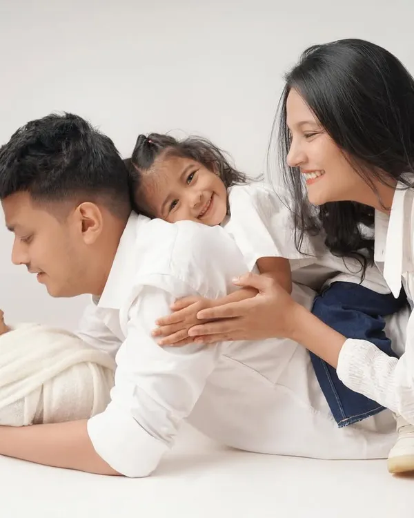 A joyful and playful family portrait with a newborn. The older sister gives her dad a hug while he holds the baby, and mom looks on with a smile. It’s a moment of pure, chaotic, beautiful family life.