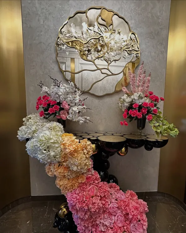 This home wedding decor features a stunning floral installation that flows from a console table and frames a doorway, using a beautiful ombre effect with pink, orange, and white flowers.