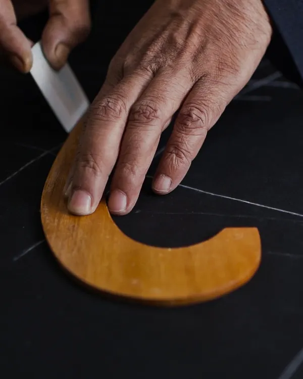 The first mark of a master craftsman. Here, our bespoke cutter uses traditional tools to chalk the pattern directly onto the fabric. This foundational step requires immense precision and an expert eye, as it dictates the final form of the garment.