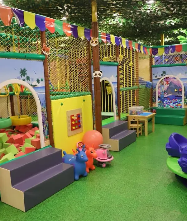 A full view of our vibrant, jungle-themed play area. You can see the foam pit, rockers, merry-go-round, and the multi-level structure, all under a canopy of faux leaves.
