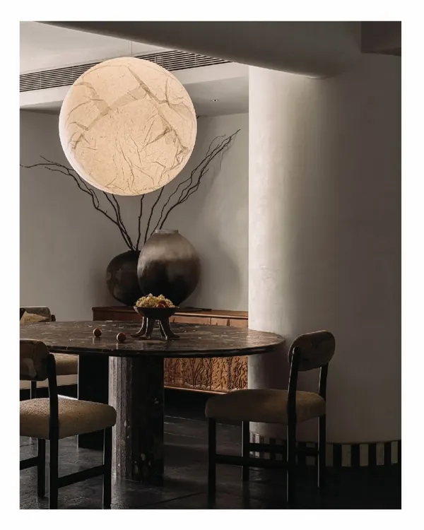 In the 'Aria' project, the dining area is an intimate space tucked behind a candle wall. We designed this African Marble monolith table, which sits under a 'Moon light' fixture, creating a dramatic and otherworldly dining experience.