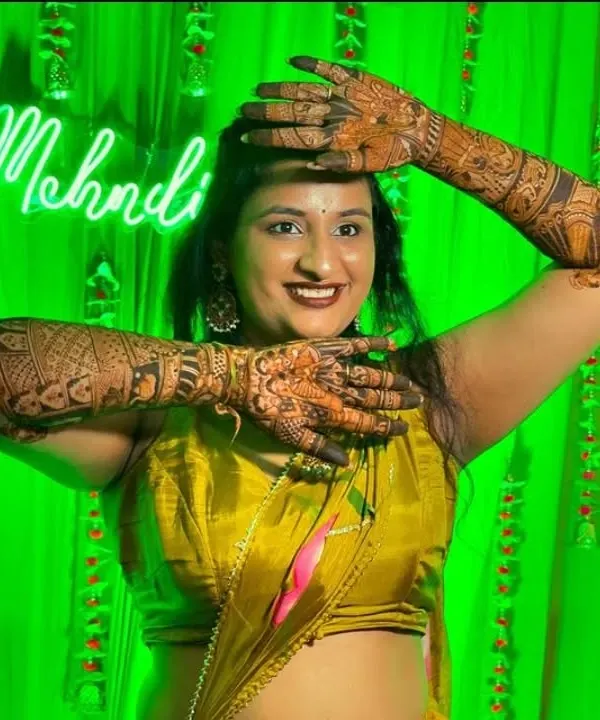 A happy bride posing with her full bridal mehendi against a festive green backdrop. Her joy and beautiful henna are what make my work so rewarding.