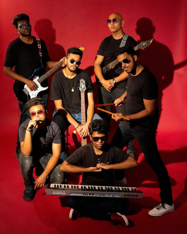 A full-group shot of a music band against a vibrant red background. This classic band promo shot establishes their collective identity and highlights their instruments, conveying energy and professionalism.